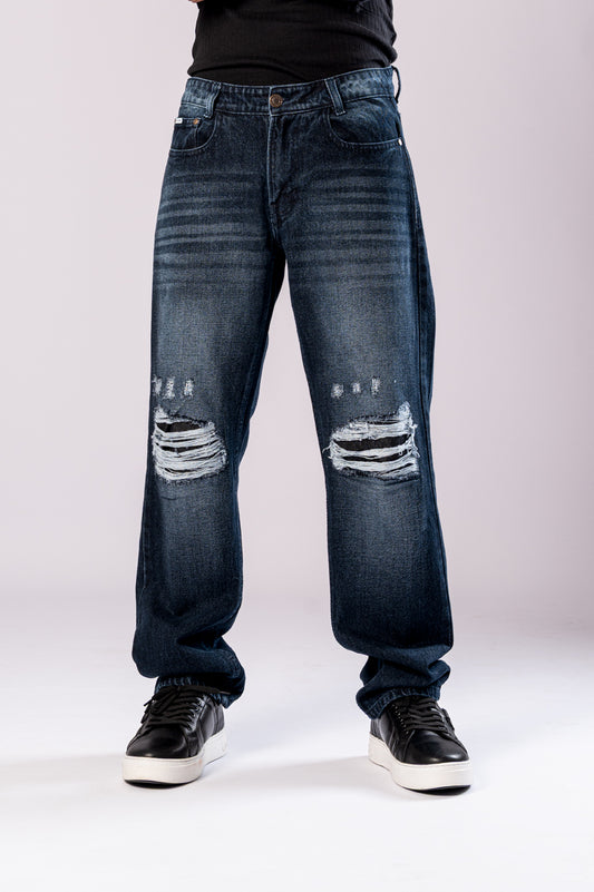 Front view of a person's lower body, showing dark-wash blue baggy jeans with ripped knees and black sneakers.