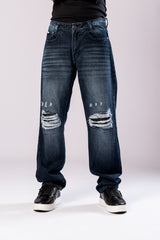 Front view of a person's lower body, showing dark-wash blue baggy jeans with ripped knees and black sneakers.