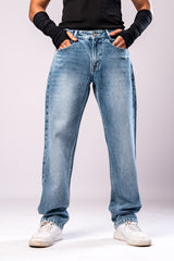 Full-body front view of a person wearing light-wash blue baggy jeans with a black top and black arm sleeves, with their hands in their pockets.