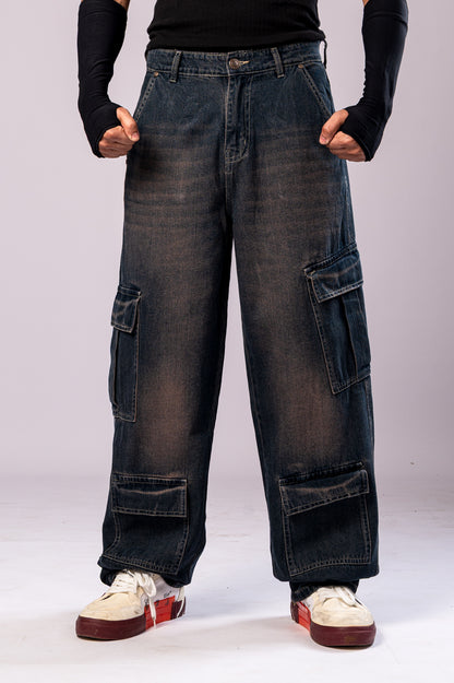 Full-body front view of a person wearing dark, rusty-blue baggy cargo jeans with a black top and black arm sleeves, with their hands clenched.