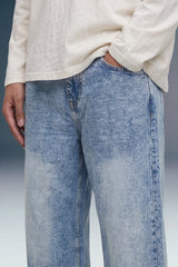 A close-up of a person wearing light blue acid-wash jeans and a cream-colored linen long-sleeve shirt, cropped from the chest down.