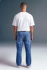 A man viewed from behind wearing a white short-sleeve t-shirt and blue jeans, standing against a dark gray studio background.