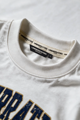 Close-up of a white crewneck t-shirt showing the inner neck label with 'UNDERRAATED' branding and the top of a navy blue and gold graphic print.