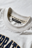 Close-up of a white crewneck t-shirt showing the inner neck label with 'UNDERRAATED' branding and the top of a navy blue and gold graphic print.