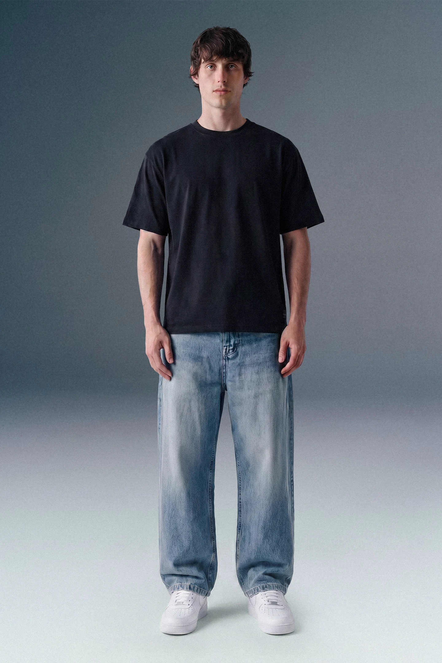 Person wearing a black t-shirt, light blue jeans, and white sneakers on a gray background