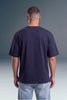 A man viewed from behind wearing a dark navy blue short-sleeve t-shirt and light blue jeans, standing against a dark gray gradient studio background.