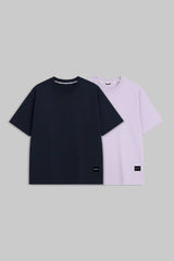 Two short-sleeve crewneck T-shirts displayed flat against a solid gray background. The front shirt is solid black, and the shirt behind it is a light lavender purple, both featuring small black rectangular labels near the bottom hem.