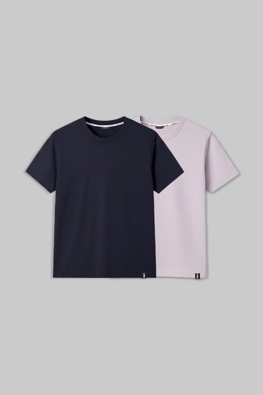 Two short-sleeve crew-neck t-shirts displayed in a flat-lay arrangement on a solid gray background. The front shirt is dark navy blue, and the shirt behind it is a light pastel lavender-pink.