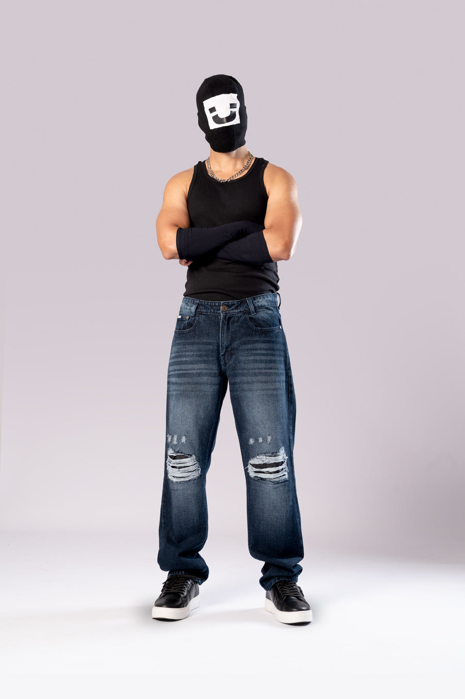 Full-body front view of a person wearing a black ski mask, a black tank top, and dark-wash blue baggy jeans with ripped knees.