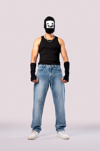 Full-body front view of a person wearing a black ski mask with a white smiley face, a black tank top, black arm sleeves, and light-wash blue baggy cargo jeans.