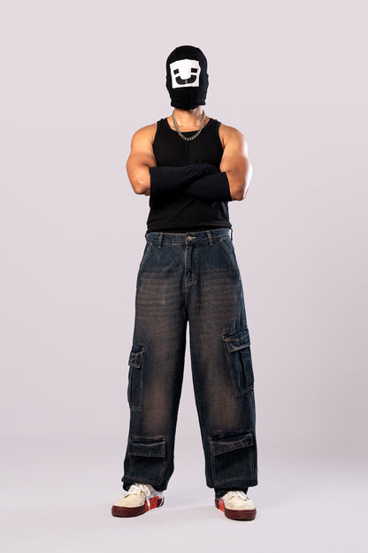 Full-body front view of a person wearing a black ski mask with a white smiley face, a black tank top, black arm sleeves, and light-wash blue baggy cargo jeans.