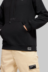 Close-up of black oversized hoodie hem featuring a small rectangular 