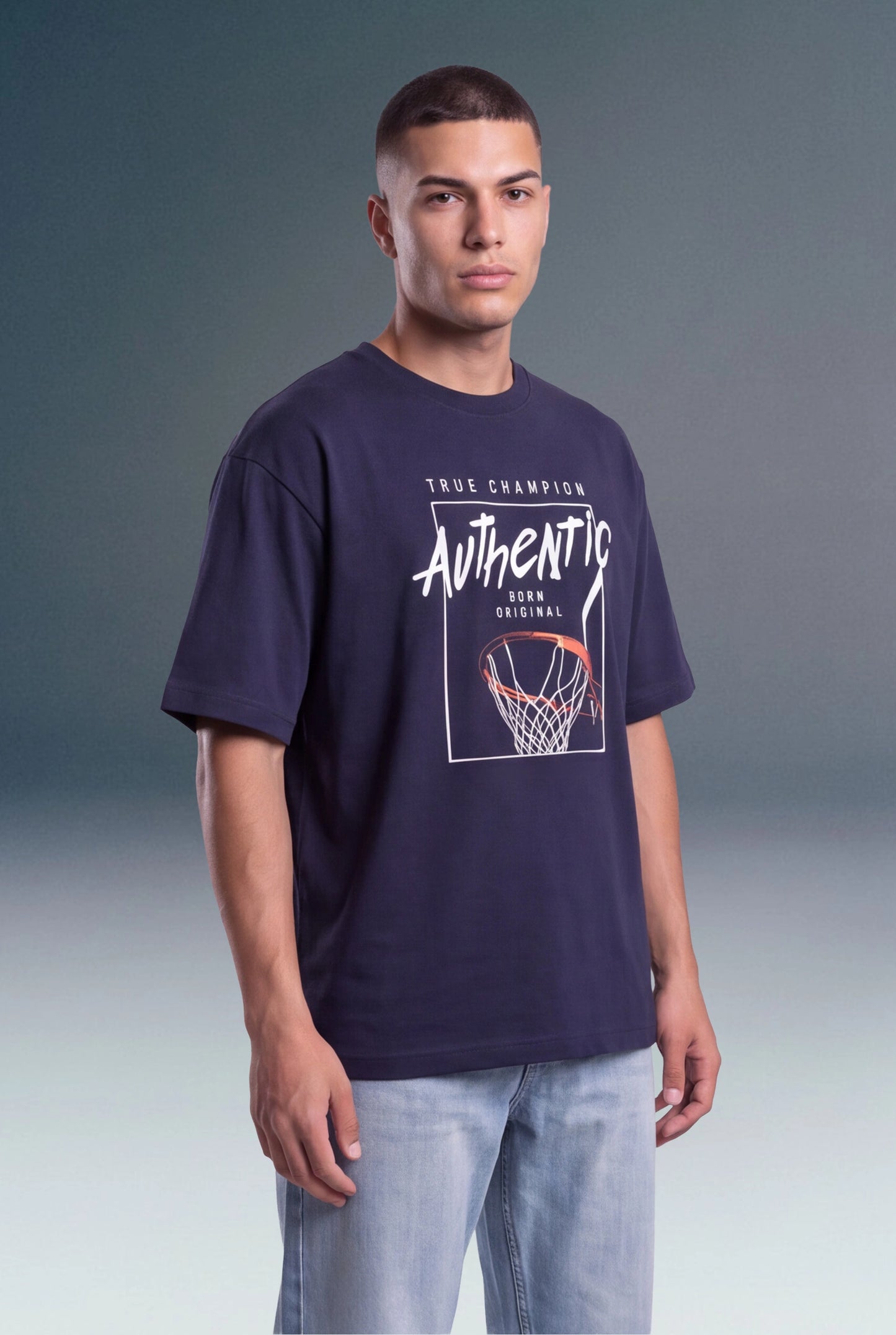 A man wearing a navy blue graphic t-shirt with a basketball hoop design and the word 'Authentic' printed on the front, paired with light blue jeans, set against a studio background.