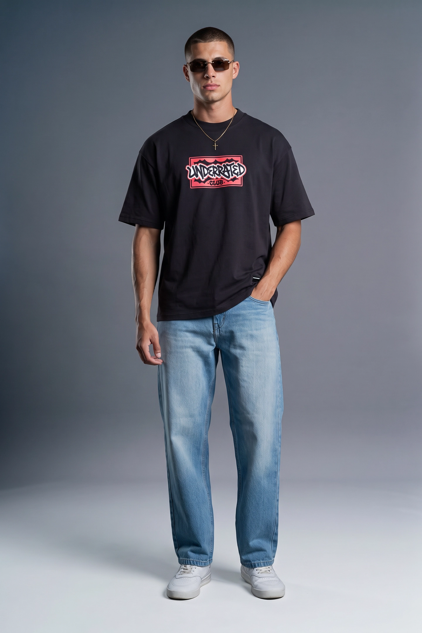 A man modeling a black short-sleeve graphic t-shirt with a red and white 'Misterio' logo, paired with light blue jeans and white sneakers, against a dark gray studio background.