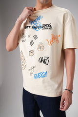 Man wearing beige printed graphic t‑shirt and dark jeans, cropped at neck, standing against plain studio background.
