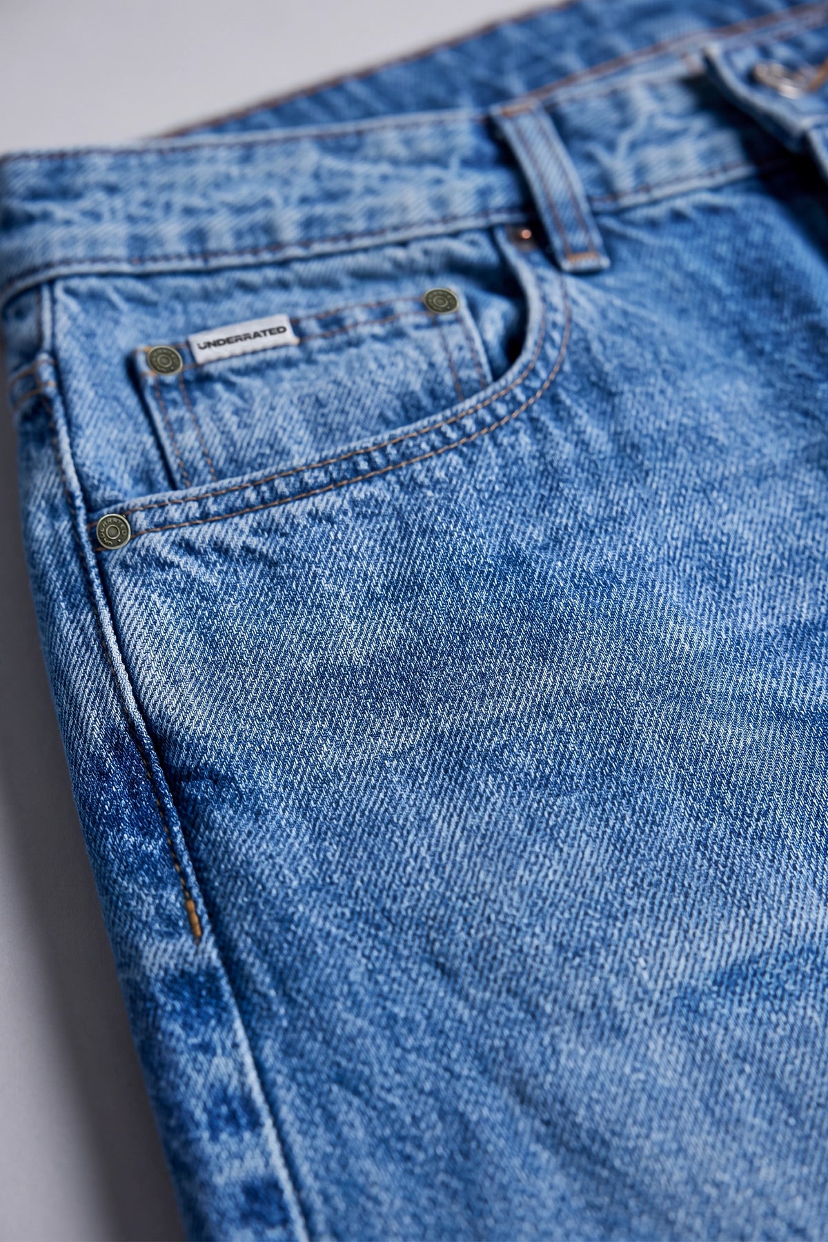Close-up of a pair of blue denim jeans showing the back pocket, button, rivets, belt loops, and faded wash texture.