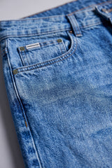 Close-up of a pair of blue denim jeans showing the back pocket, button, rivets, belt loops, and faded wash texture.