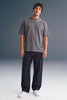 Full-length front view of a man standing straight against a grey studio backdrop, wearing a dark grey T-shirt, loose dark navy trousers, and white sneakers.