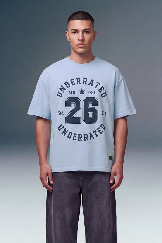 A male model wearing a light blue t-shirt with a dark navy graphic print that reads 'UNDERRATED ATH. DEPT.