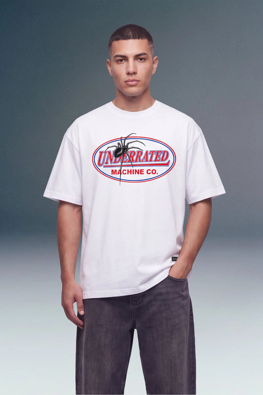 A man wearing a white crewneck t-shirt with a red and blue 'Unbranded Machine Co.' graphic on the chest, paired with dark gray jeans, against a studio background.
