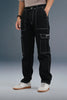 Close-up of the front of black cargo pants, emphasizing the white stitching and large side pockets.