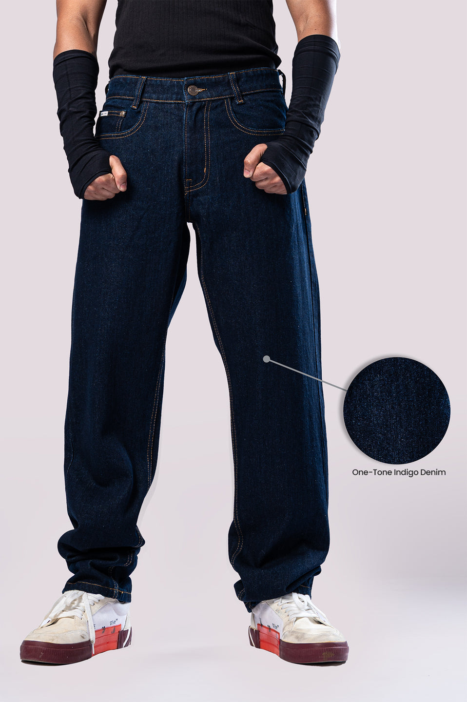 Front view of a person wearing dark-wash blue baggy jeans, with a circular inset magnifying the "One-Tone Indigo Denim" fabric.