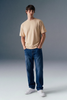 Man wearing a beige t-shirt, blue jeans, and white sneakers against a gray background
