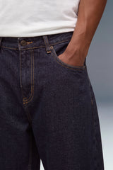 Close-up of a person wearing dark indigo denim jeans with a white t-shirt, showing the front pocket and side pocket details.