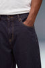 Close-up of a person wearing dark indigo denim jeans with a white t-shirt, showing the front pocket and side pocket details.