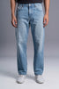 A person wearing light blue straight-leg denim jeans with a faded wash, paired with a black top and white sneakers, shown from the waist down against a gray studio background.