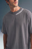 Medium close-up shot from the chest up of a man looking to the side, wearing a dark grey crewneck T-shirt with small white text printed along the left side of the collar.