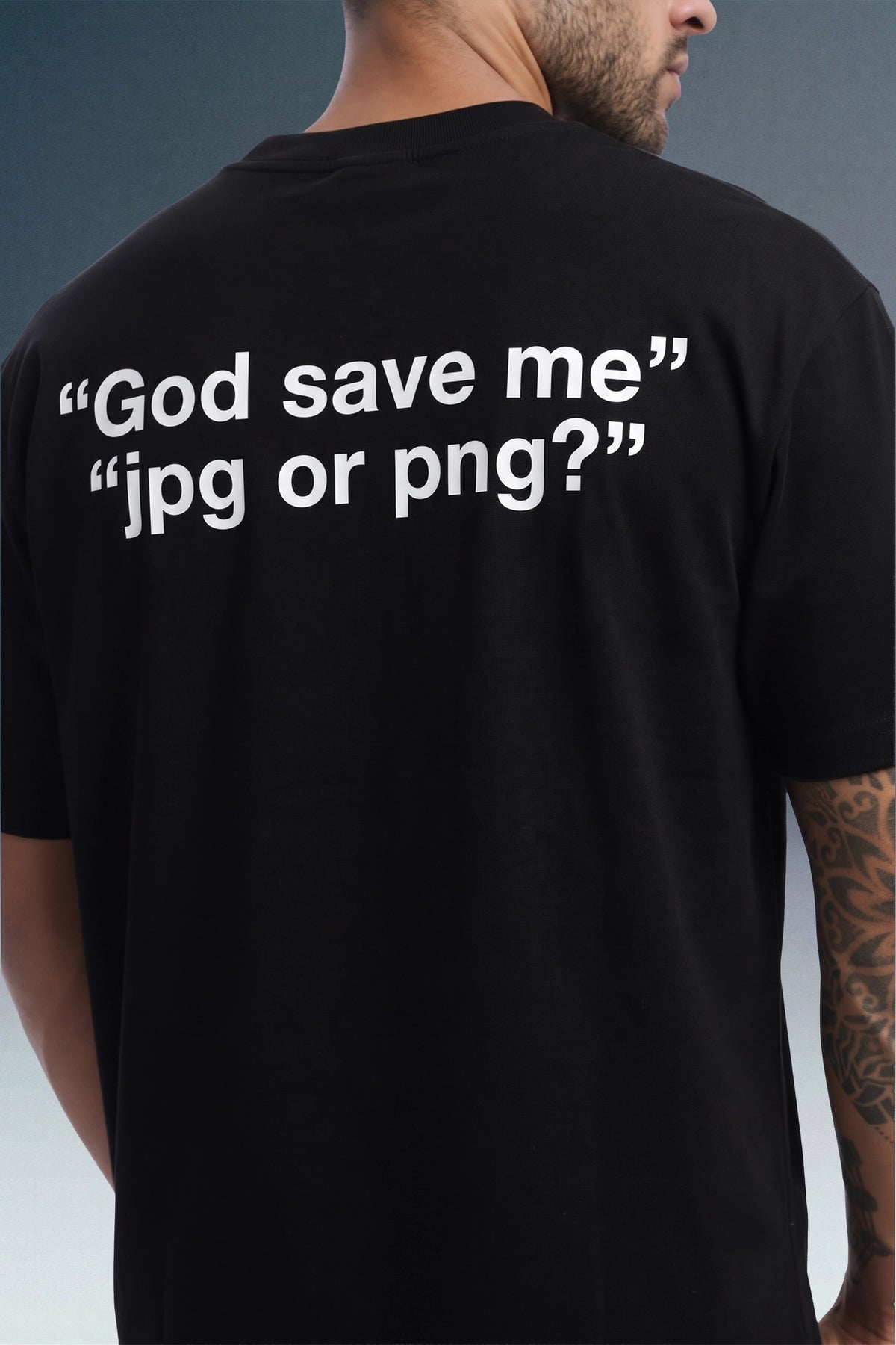 A man wearing a black t-shirt, viewed from the back. The shirt features the white printed text '"God save me" "jpg or png?"' on the back.