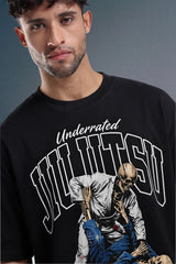 A man wearing a black graphic t-shirt with 'Underrated Jiu Jitsu' and a skeleton fighting illustration on the front, set against a dark gray studio background.