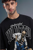 A man wearing a black graphic t-shirt with 'Underrated Jiu Jitsu' and a skeleton fighting illustration on the front, set against a dark gray studio background.
