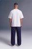 A man viewed from behind wearing a plain white short-sleeve t-shirt and dark navy blue jeans, standing against a gray studio background.