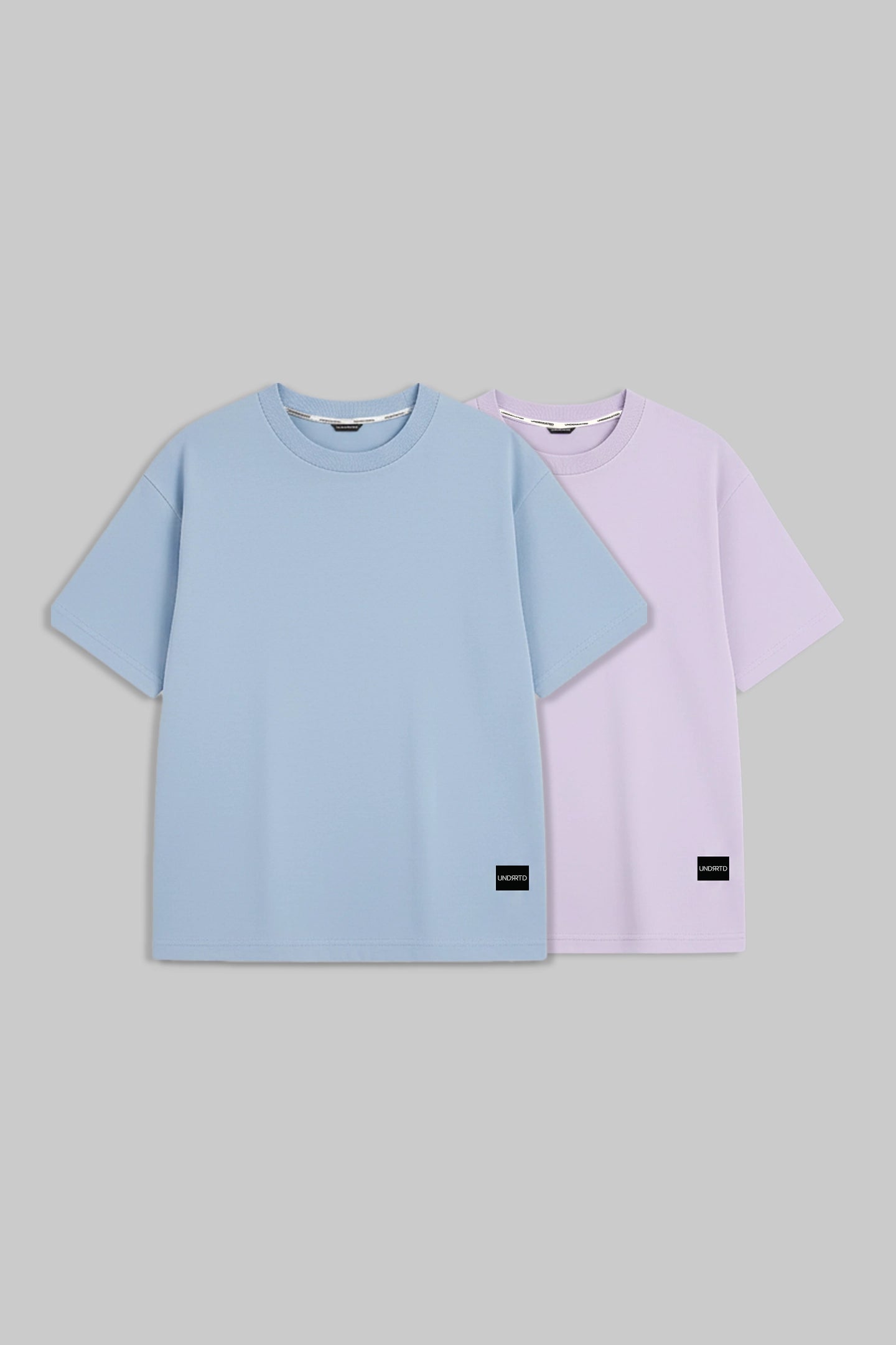 Two short-sleeve crewneck t-shirts in light blue and light purple, displayed side-by-side on a solid gray background.
