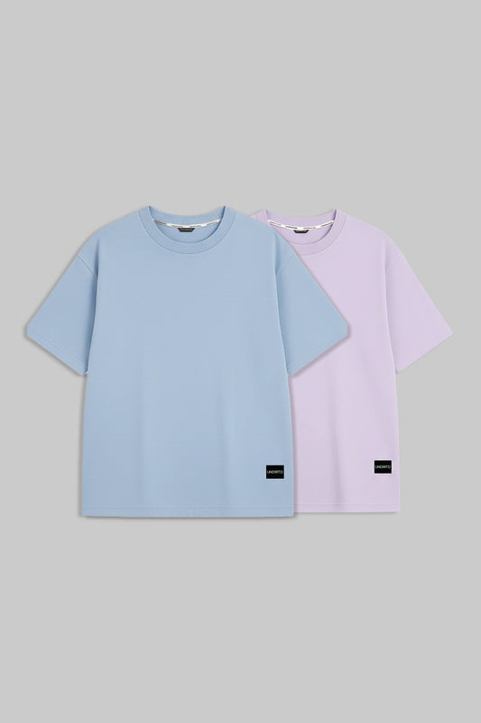 Two short-sleeve crewneck t-shirts in light blue and light purple, displayed side-by-side on a solid gray background.