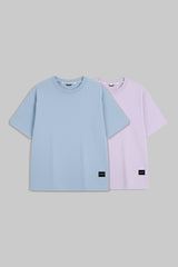 Two short-sleeve crewneck t-shirts in light blue and light purple, displayed side-by-side on a solid gray background.