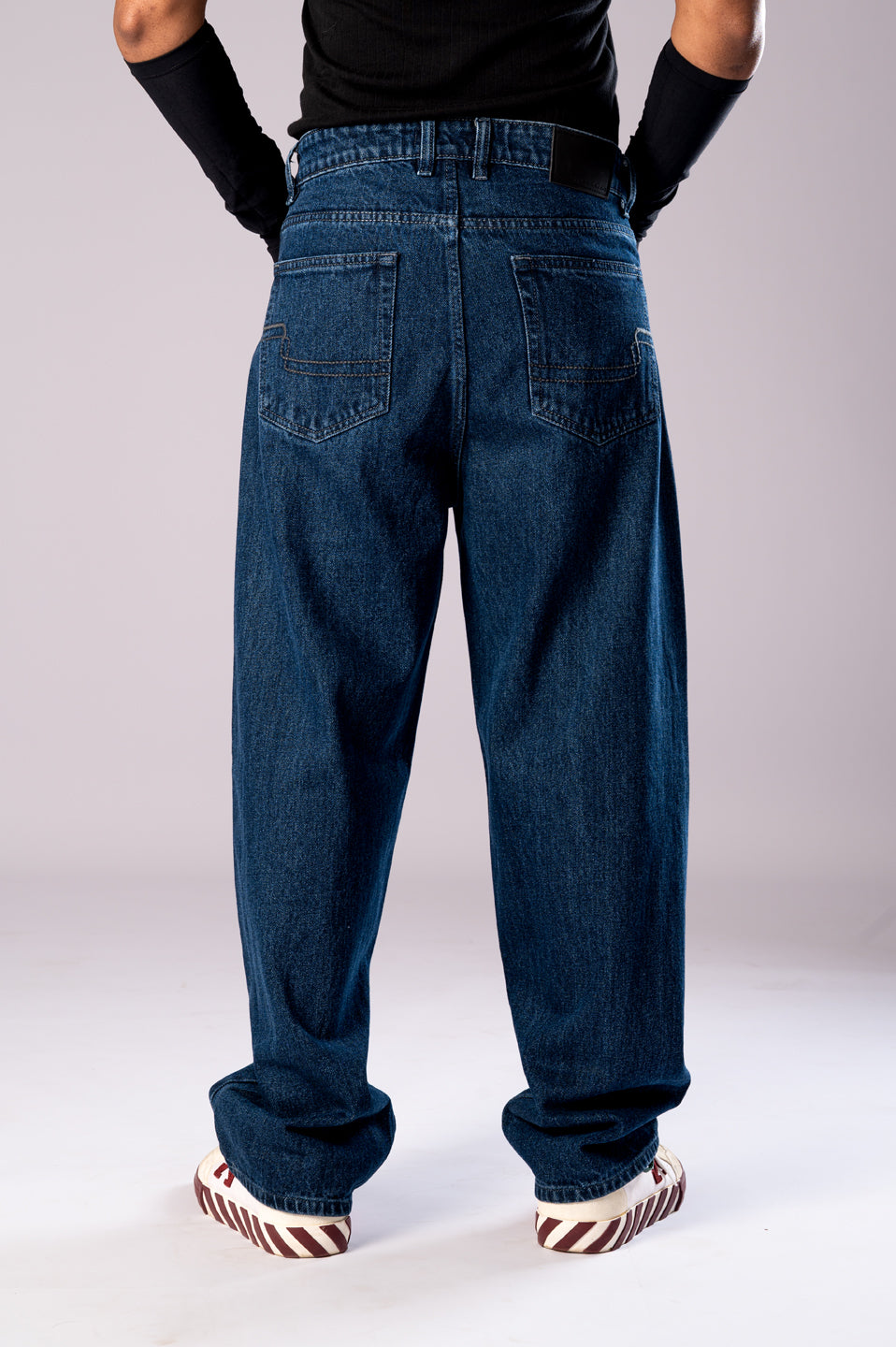 Full-body back view of a person wearing baggy, dark blue jeans, showing how they fit from behind.