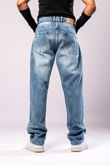 Full-body back view of a person wearing light-wash blue baggy jeans with faded and distressed details on the back pockets, a black top, and black arm sleeves.