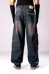 Full-body back view of a person wearing dark, rusty-blue baggy cargo jeans, a black top, and black arm sleeves, showing the loose fit and large side cargo pockets.