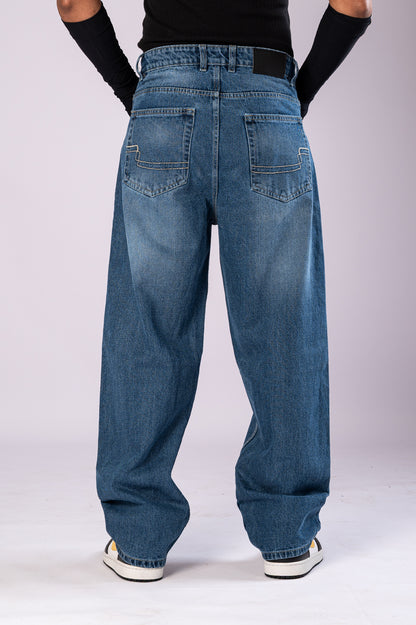 Full-body front view of a person wearing light-wash blue baggy jeans, a black top, and black arm sleeves, with their hands in their pockets.