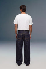 A man viewed from behind wearing a plain white short-sleeve t-shirt and dark wide-leg denim jeans, standing against a studio background with a blue-to-gray gradient.