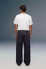 A man viewed from behind wearing a plain white short-sleeve t-shirt and dark wide-leg denim jeans, standing against a studio background with a blue-to-gray gradient.