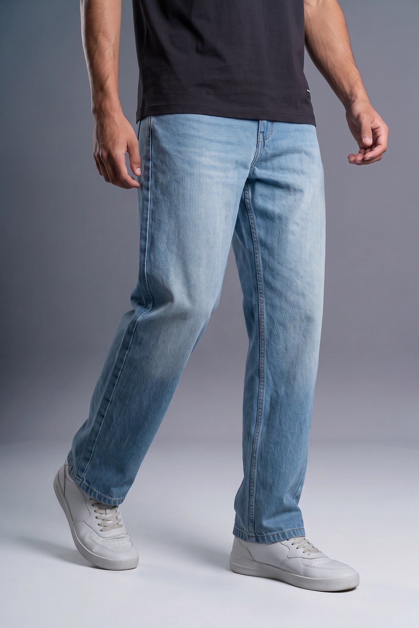 A person wearing light blue straight-leg jeans, a black t-shirt, and white sneakers, shown from the waist down against a gray studio background.