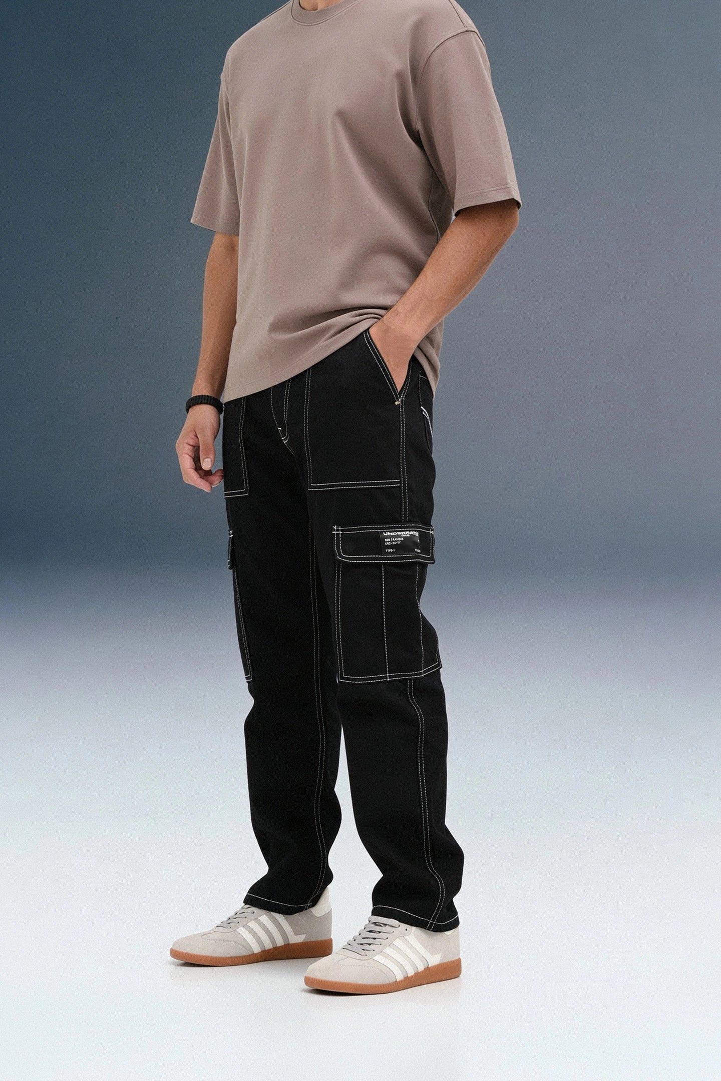 A person standing at an angle in black contrast-stitch cargo pants against a grey background.
