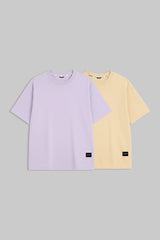 Two short-sleeve crewneck t-shirts displayed side by side on a solid gray background. The front t-shirt is light lavender purple, and the t-shirt behind it is pale yellow.