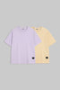Two short-sleeve crewneck t-shirts displayed side by side on a solid gray background. The front t-shirt is light lavender purple, and the t-shirt behind it is pale yellow.