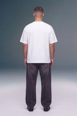 A man viewed from behind wearing a plain white short-sleeve t-shirt and dark gray wide-leg jeans, standing against a studio background with a gray-to-white gradient.