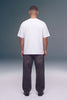 A man viewed from behind wearing a plain white short-sleeve t-shirt and dark gray wide-leg jeans, standing against a studio background with a gray-to-white gradient.